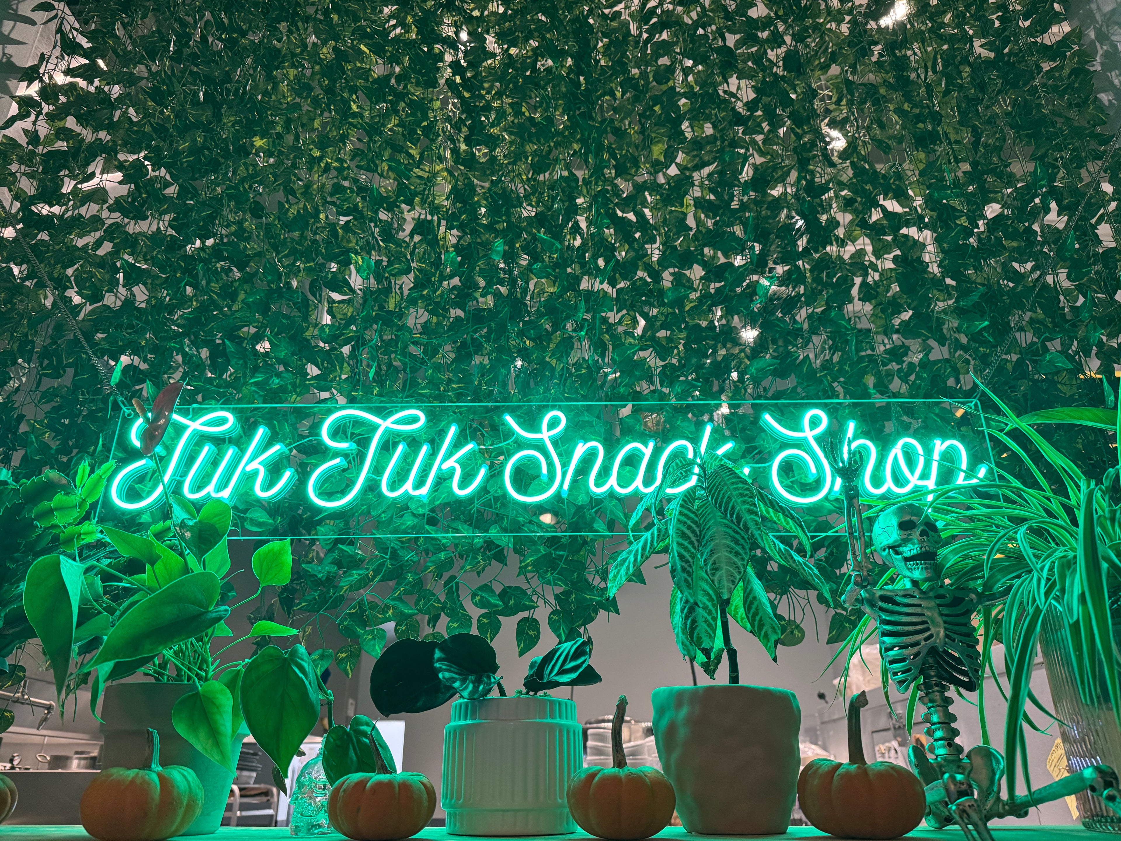 Neon sign reading Tuk Tuk Snack Shop nestled among greenery.